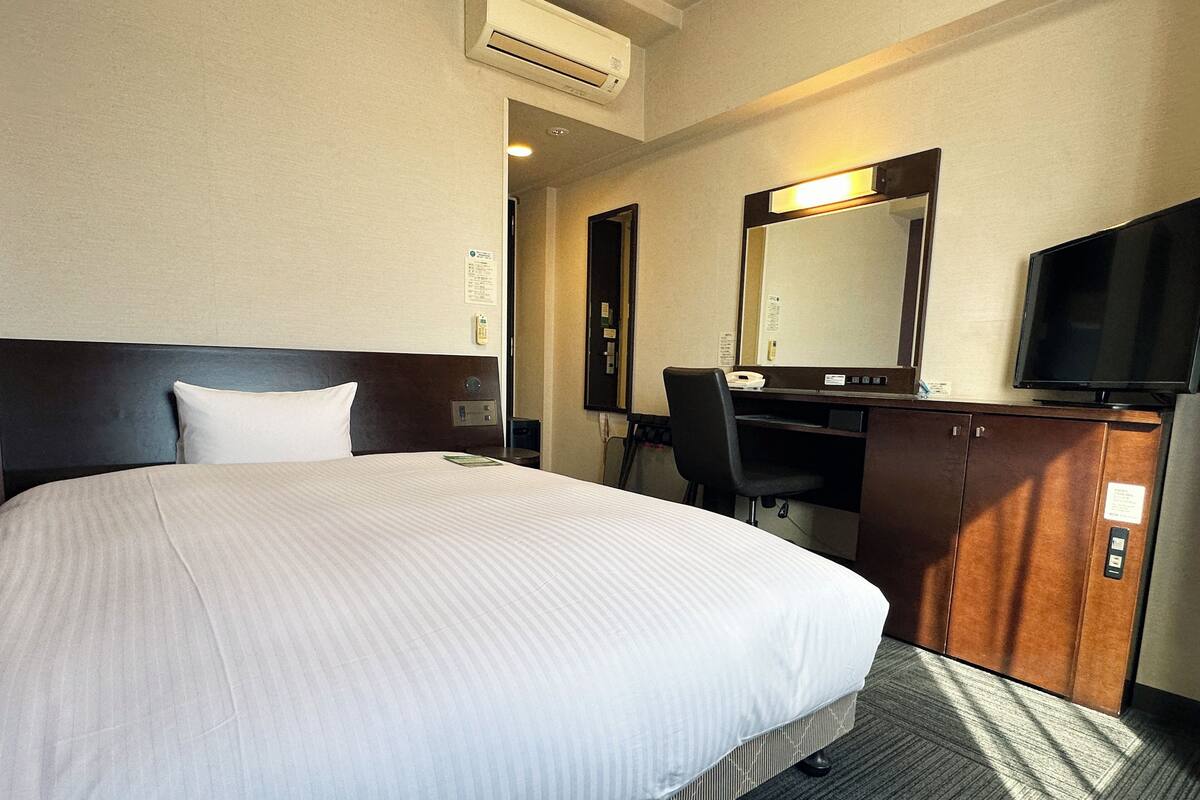 A hotel room with a large bed, a desk with a chair, a television, and a mirror.