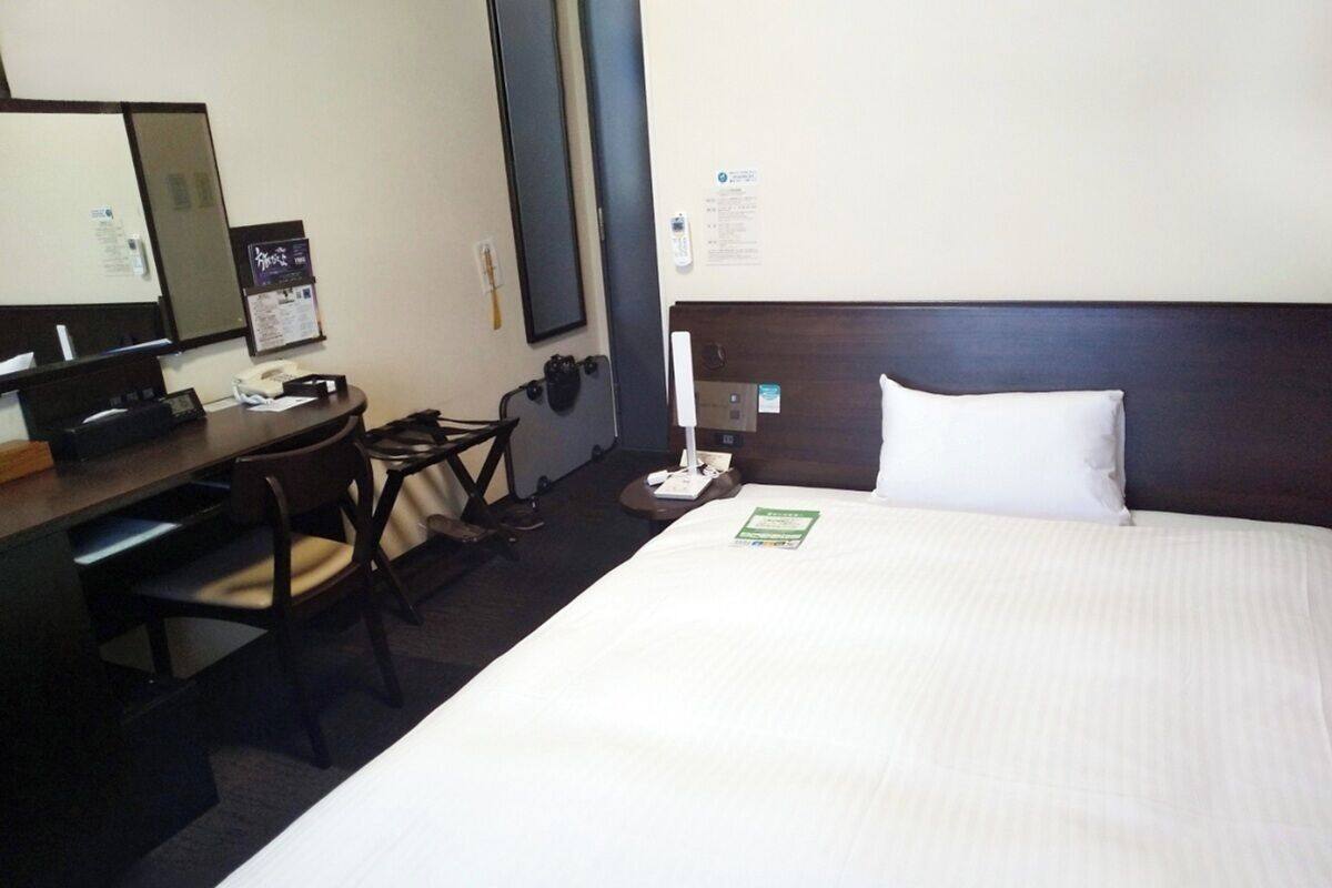 Habitació d'hotel amb un llit gran, un escriptori amb una cadira, un telèfon i un mirall.