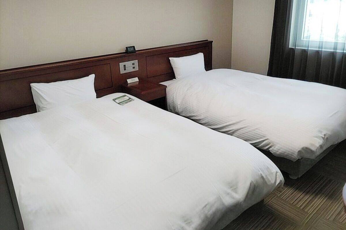 Habitació d'hotel amb dos llits individuals, ambres de fusta, una tauleta de nit i una finestra amb cortines.