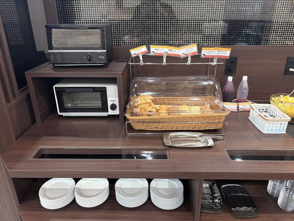 A breakfast station with a toaster, microwave, and a basket of bread.