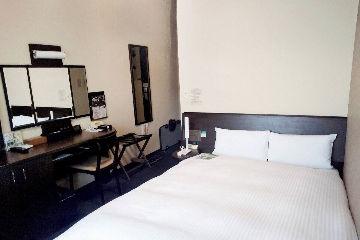 Habitació d'hotel amb un llit gran, una taula de treball amb una cadira, un mirall i una tauleta de nit.