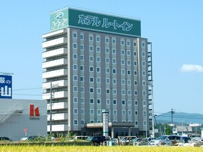 Un hotel de varios pisos con un letrero llamativo en la parte superior, un estacionamiento al frente y vistas del entorno.