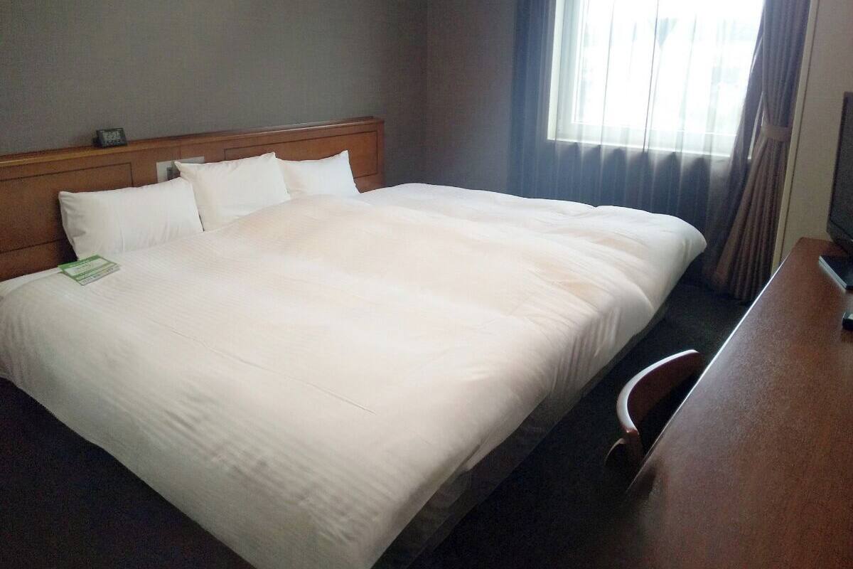 Una habitació d'hotel amb un llit gran, un panell de fusta al capçal, una taula i una finestra amb cortines.
