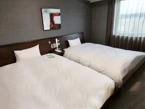 Habitación de hotel con dos camas, una mesita de noche con lámpara, una obra de arte en la pared y una ventana con cortinas.