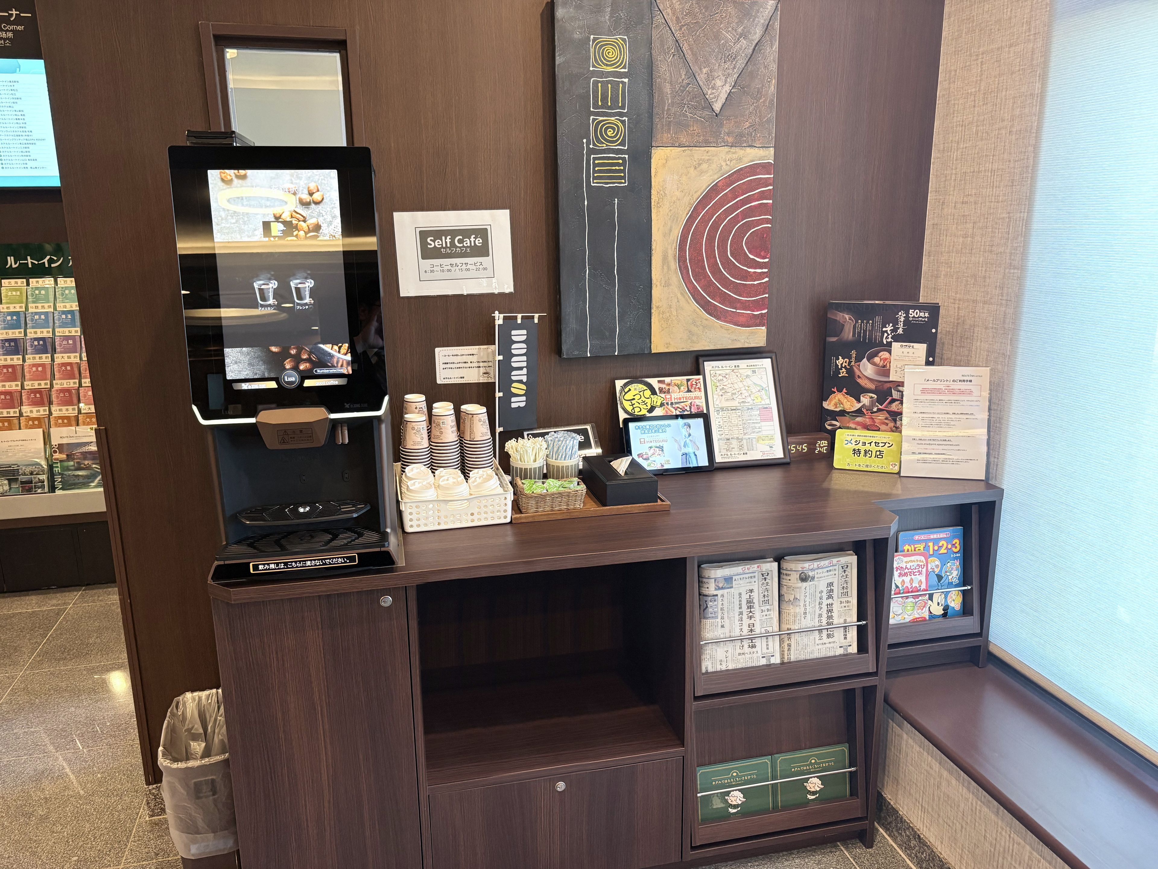 A self-service coffee station with a coffee machine, cups, and a menu board.