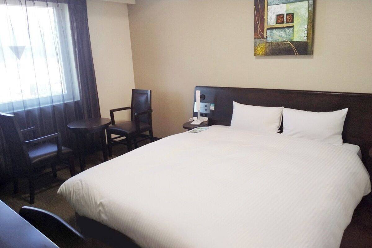 Habitació d'hotel amb un llit gran, una escriptori, una cadira i una tauleta de nit amb una làmpada.