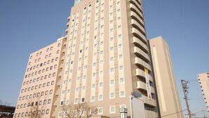 A multi-story hotel with a beige facade, numerous windows, and a green sign at the top. - Hotel Route Inn Gifu Hashima Ekimae (Hashima)