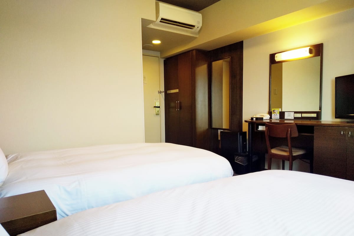 Ein Hotelzimmer mit zwei Betten, einem Schreibtisch, einem Stuhl, einem Spiegel und einer Klimaanlage.
