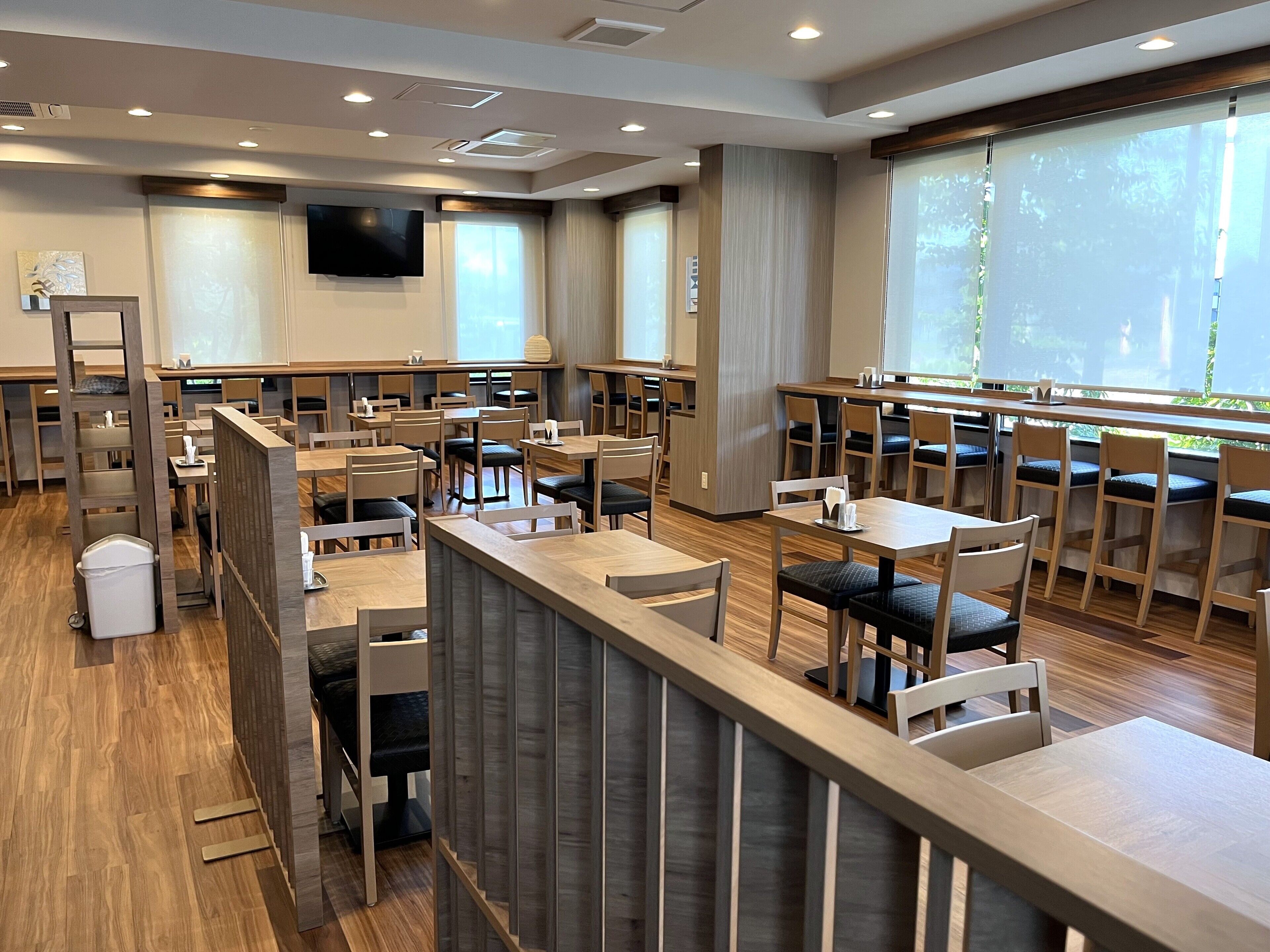 Un restaurante moderno con mobiliario de madera, un televisor de pantalla plana y ventanas amplias.