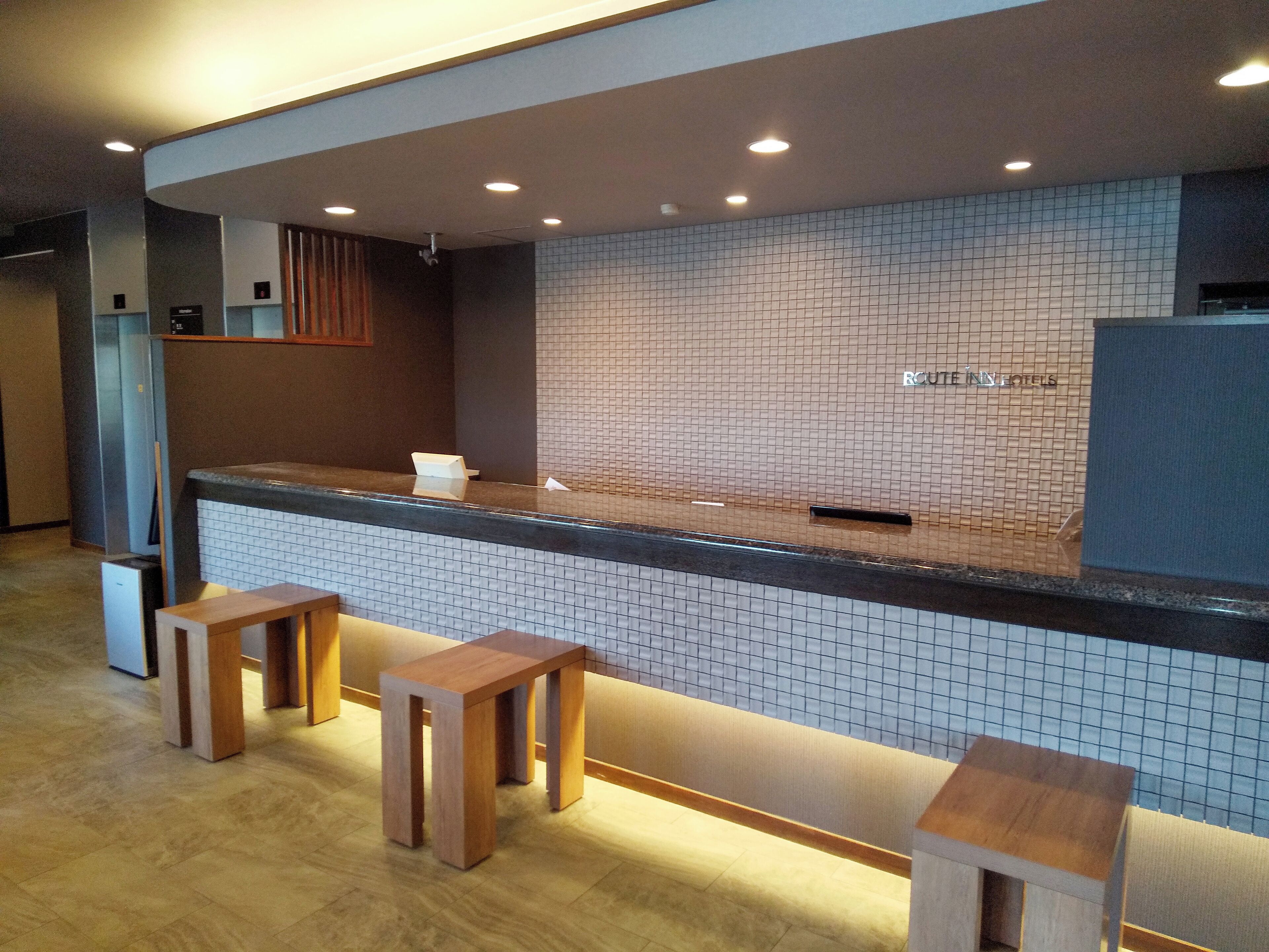 Un área de recepción con pared de azulejos, mostrador y dos taburetes de madera.