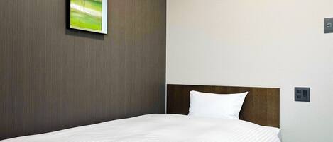 A hotel room with a bed, a headboard, a wall-mounted light switch, and a painting of flowers.