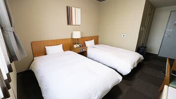 Habitación de hotel con dos camas, una mesita de noche con lámpara, teléfono y un pequeño cuadro en la pared.