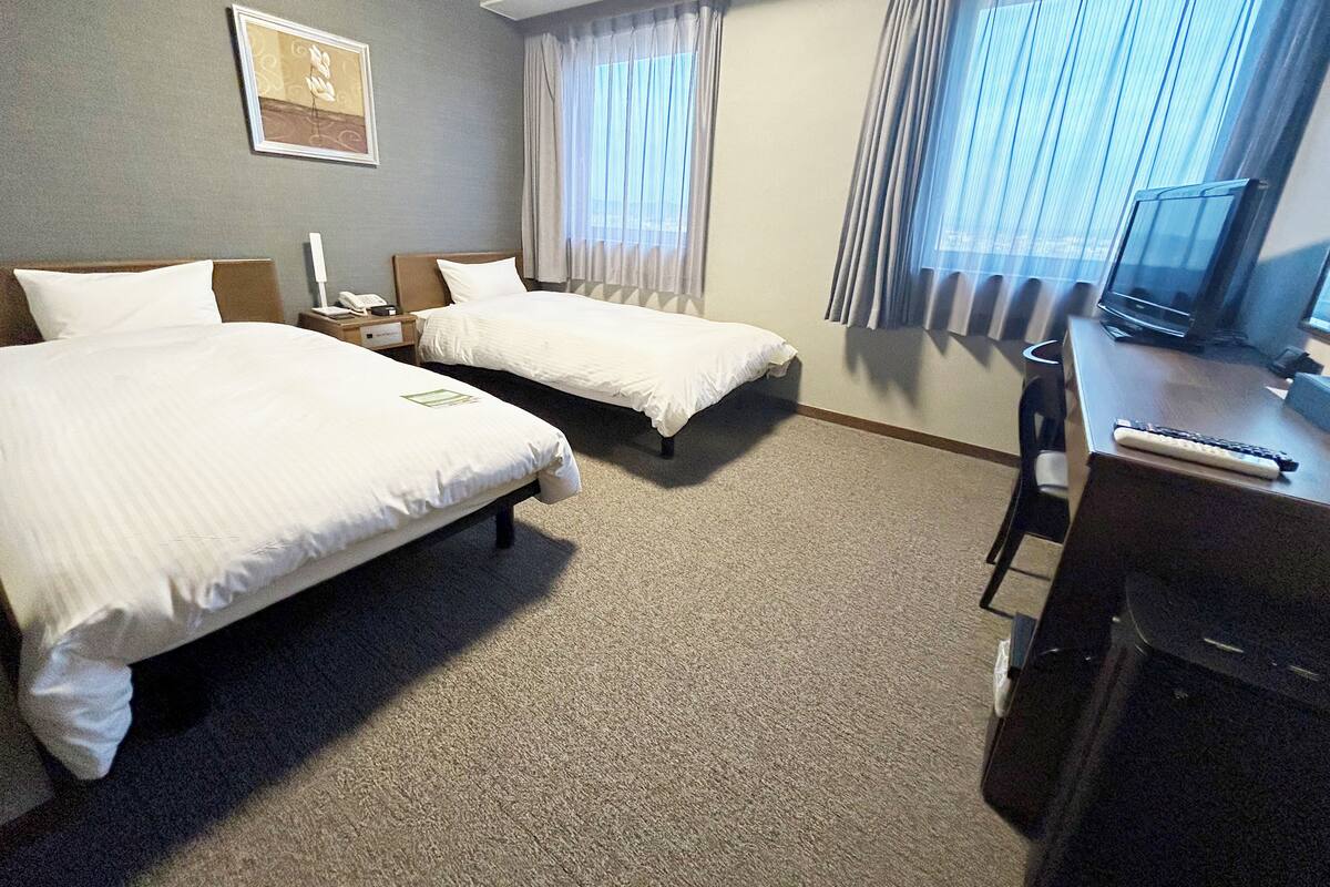 A hotel room with two beds, a desk with a computer, a chair, and a window with curtains.