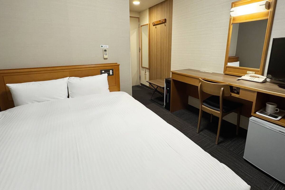 A hotel room with a bed, desk, chair, television, and a small refrigerator.