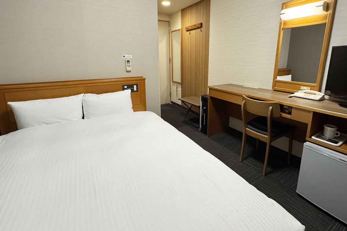 A hotel room with a bed, desk, chair, television, and a small refrigerator.