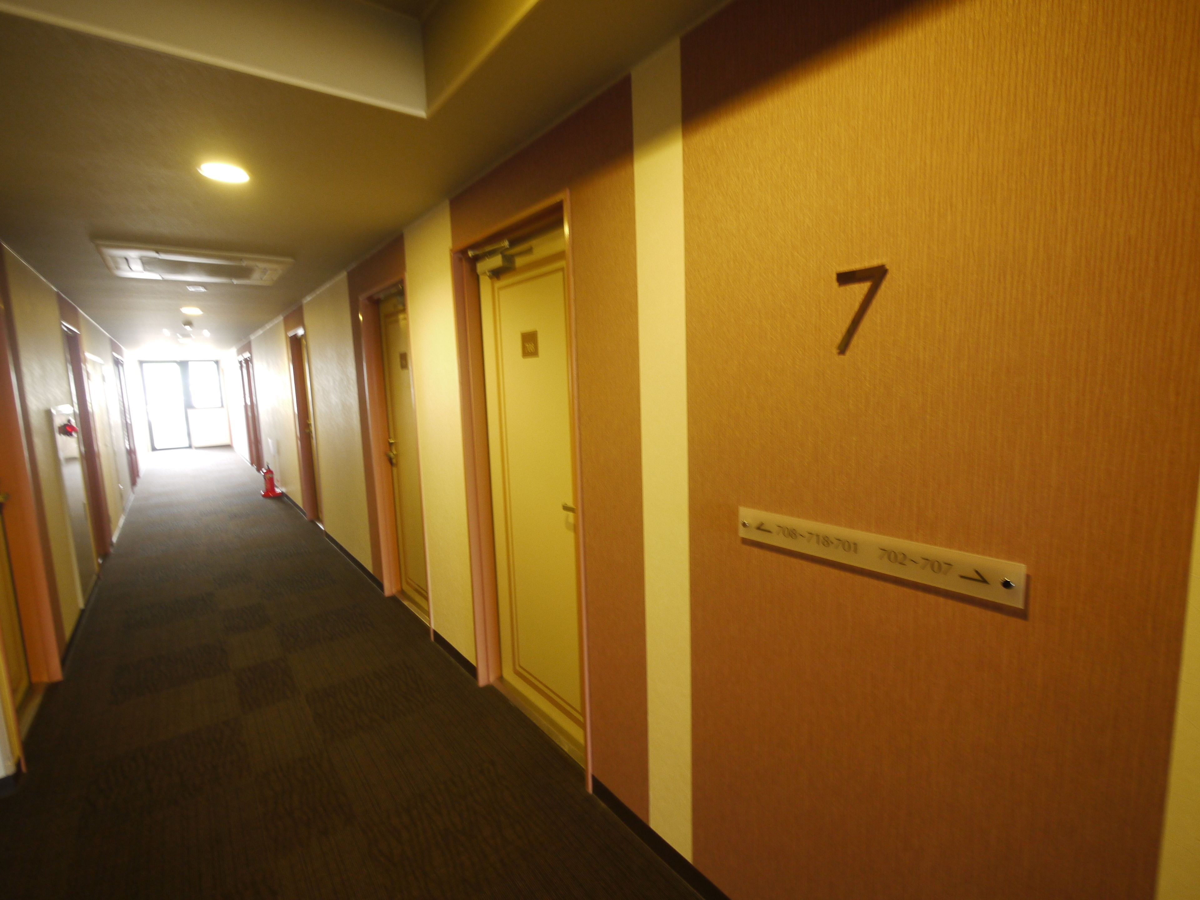 A hotel hallway with doors numbered 7 and 702-707, a fire extinguisher, and a sign with phone numbers.