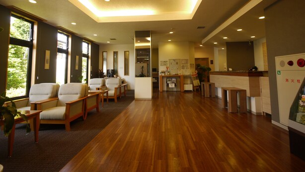 A hotel lobby with wooden flooring, seating area, reception desk, and large windows. - Hotel Route-Inn Nakatsugawa Inter (Nakatsugawa)