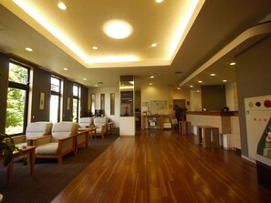 Un vestíbulo de hotel con suelo de madera, zona de estar, mostrador de recepción y amplias ventanas.