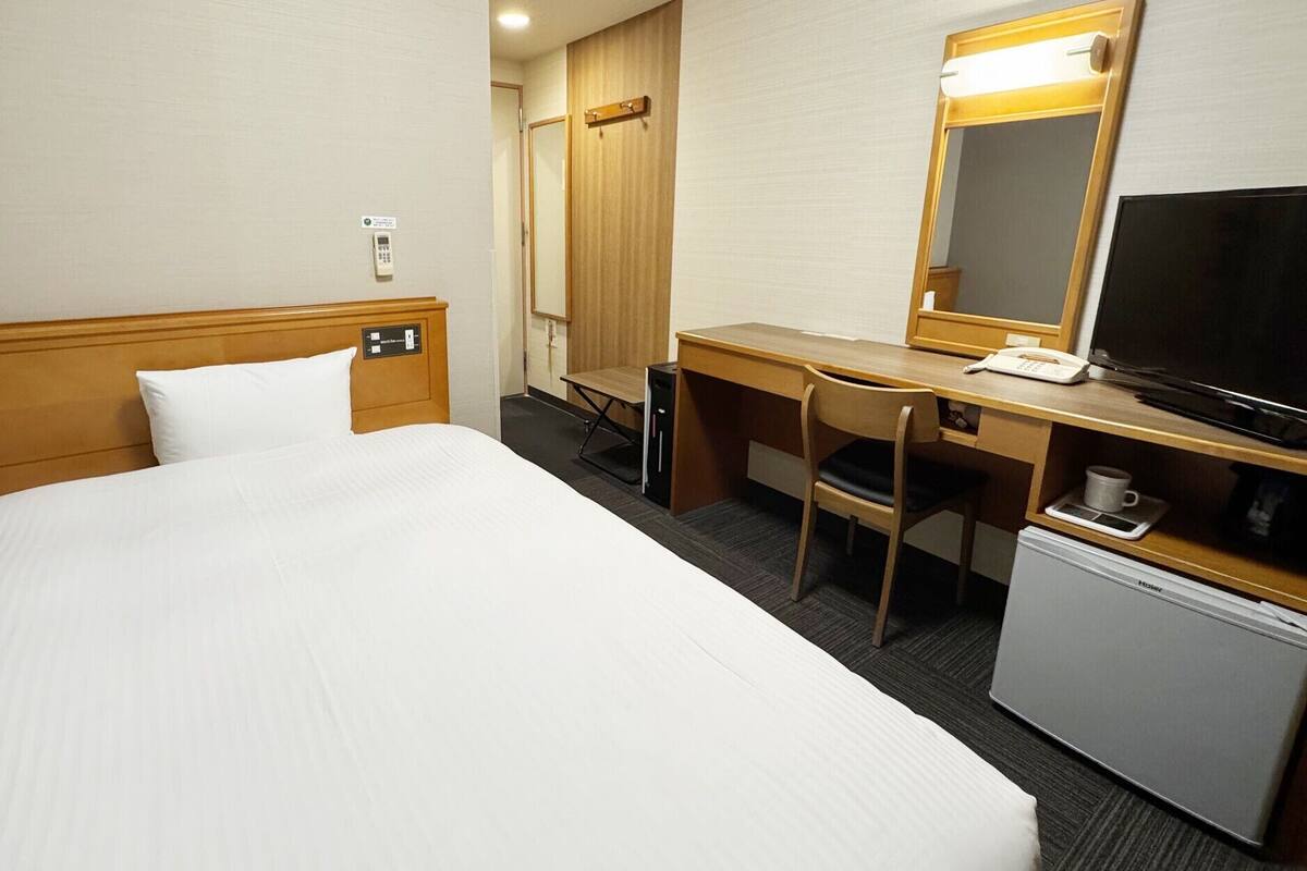 A hotel room with a bed, a desk, a chair, a television, and a small refrigerator.
