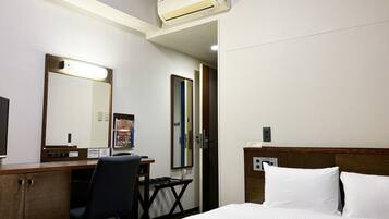 Een hotelkamer met een bed, een bureau, een stoel, een spiegel en een airconditioning.