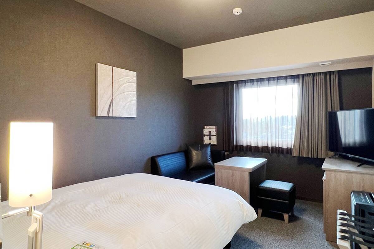 A hotel room with a large bed, a desk, a chair, a television, and a window with curtains.