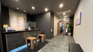 A modern hotel lobby with a reception desk, wooden stools, a seating area, and a potted plant. - Hotel Route-Inn Seki (Seki)