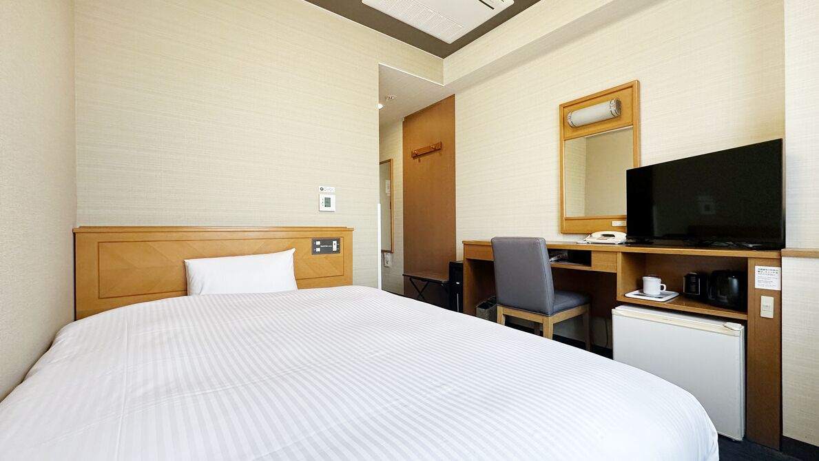 Habitación de hotel con cama, escritorio, televisor, cafetera y refrigerador.
