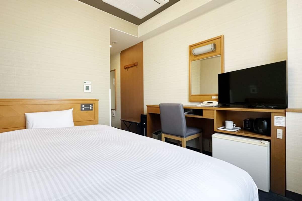 A hotel room with a bed, a desk, a television, a coffee maker, and a refrigerator.