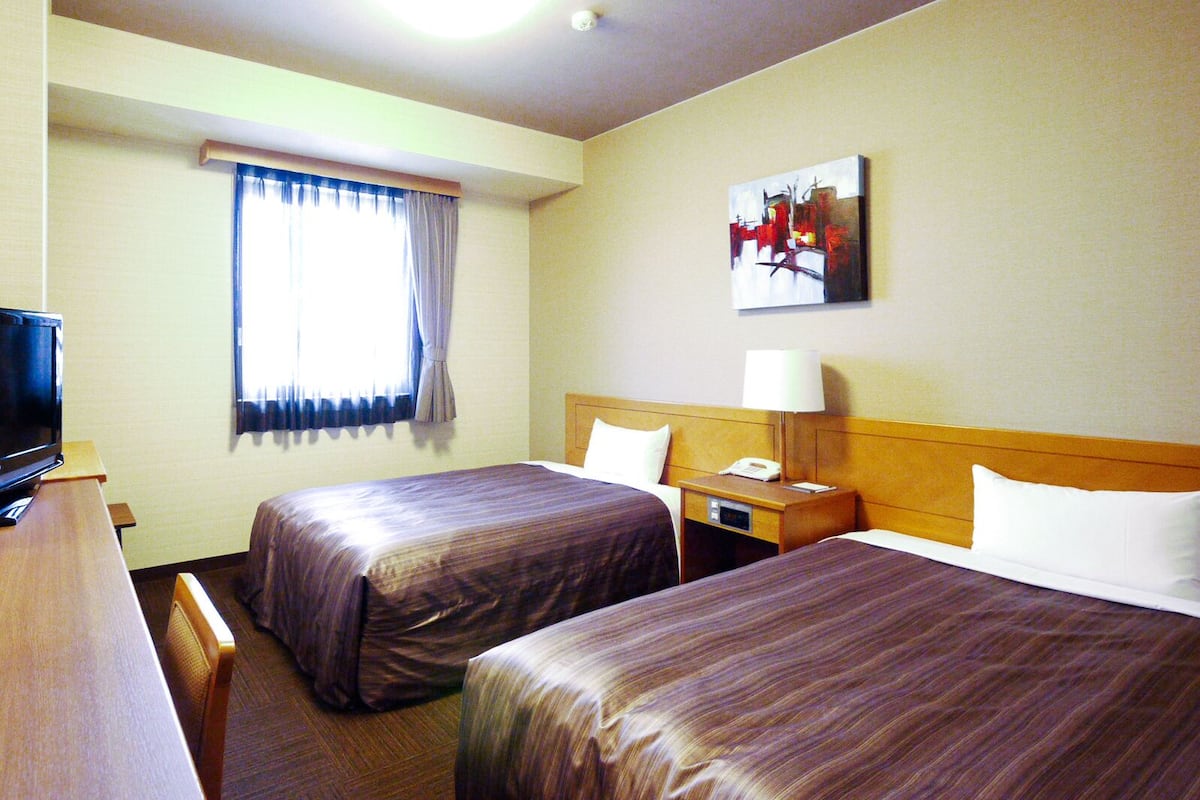 A hotel room with two beds, a desk, a television, and a painting on the wall.