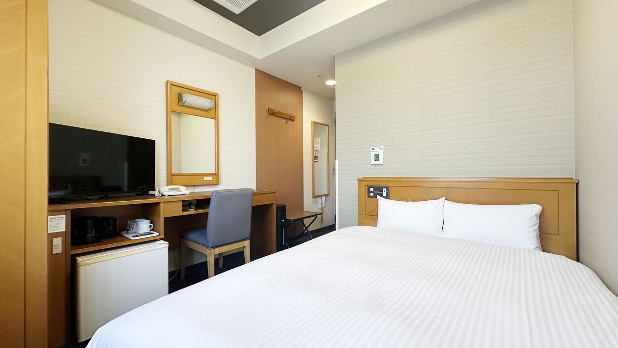 Habitación de hotel con cama, escritorio con computadora, silla, refrigerador pequeño y televisión.
