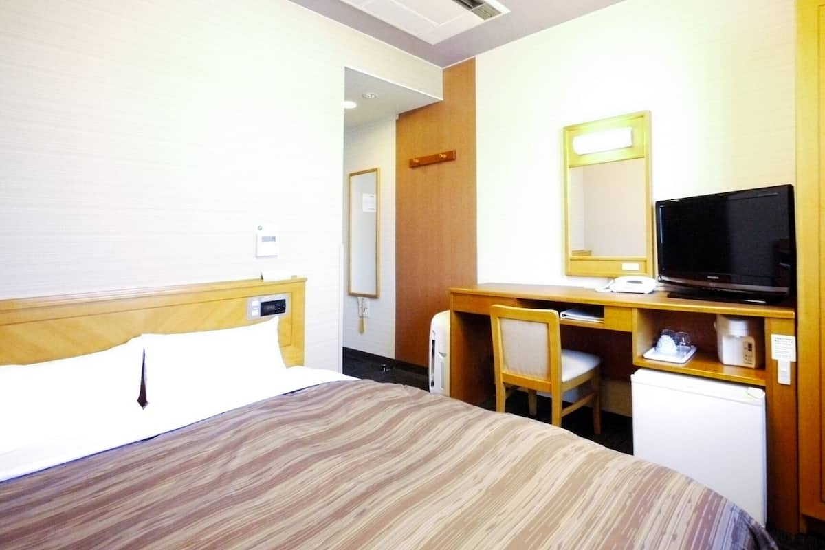 A hotel room with a bed, a desk with a chair, a television, and a small refrigerator.