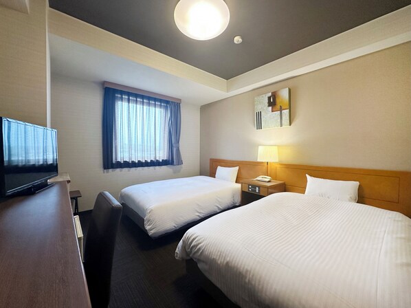 A hotel room with two beds, a desk with a television, a window with curtains, a bedside lamp, and a painting on the wall.