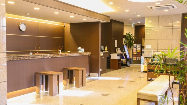 A hotel reception area with a marble counter, wooden stools, a bench, and a clock on the wall. - Hotel Route Inn Toki (Toki)