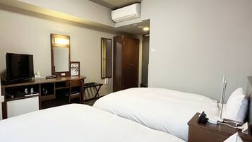 A hotel room with two beds, a desk with a TV, a mirror, and an air conditioning unit.