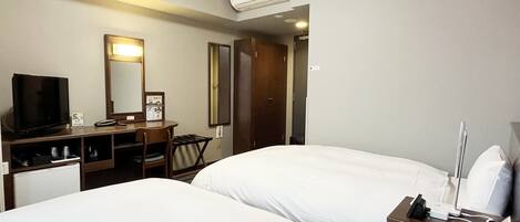 A hotel room with two beds, a desk with a TV, a mirror, and an air conditioning unit.