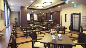 A hotel lobby with multiple dining tables and chairs, a reception area, and a staircase leading to an upper floor. - Hotel Route Inn Toki (Toki)