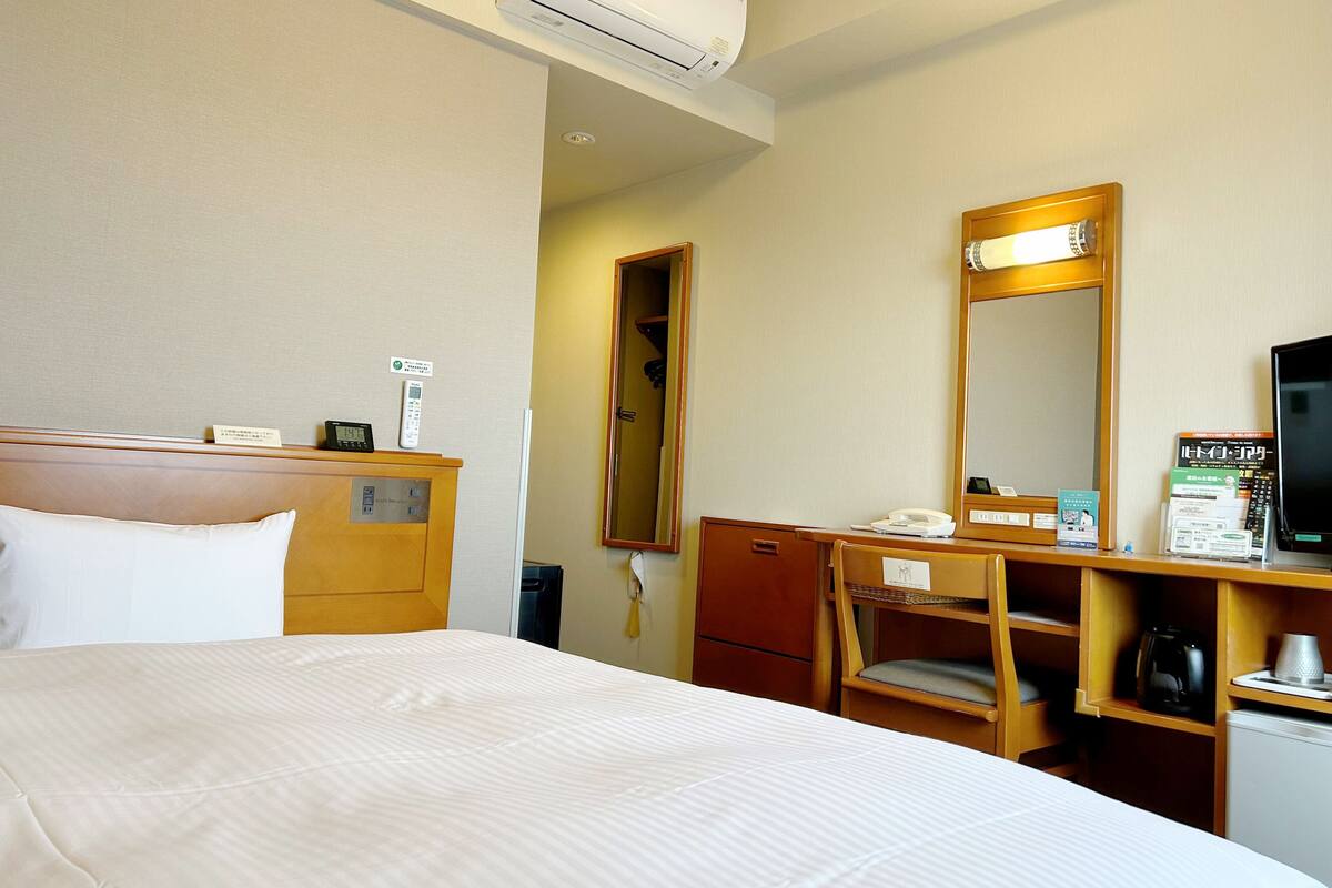 A hotel room with a bed, a desk with a telephone, a mirror, and a coffee maker.