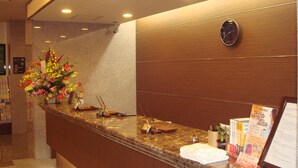 Mostrador de recepción de hotel con un reloj, un arreglo floral y folletos informativos.