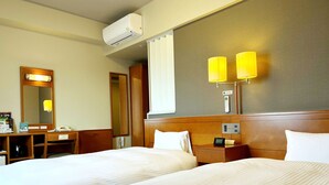 Habitación de hotel con dos camas, un escritorio, un espejo, una mesita de noche con lámpara y un equipo de aire acondicionado.