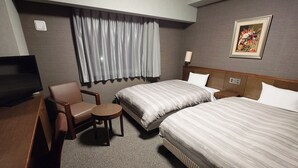 Habitación de hotel con dos camas, un escritorio, una silla, una mesita, televisor y ventana con cortinas.