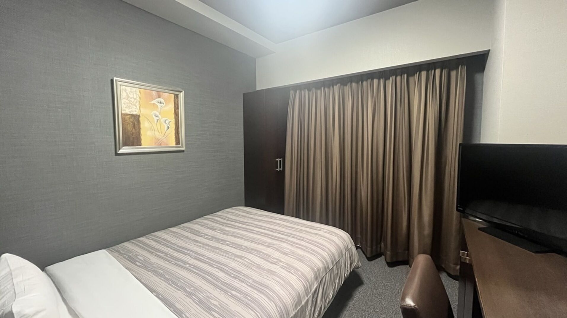 A hotel room with a bed, a desk, a chair, a television, a door, and a curtain.