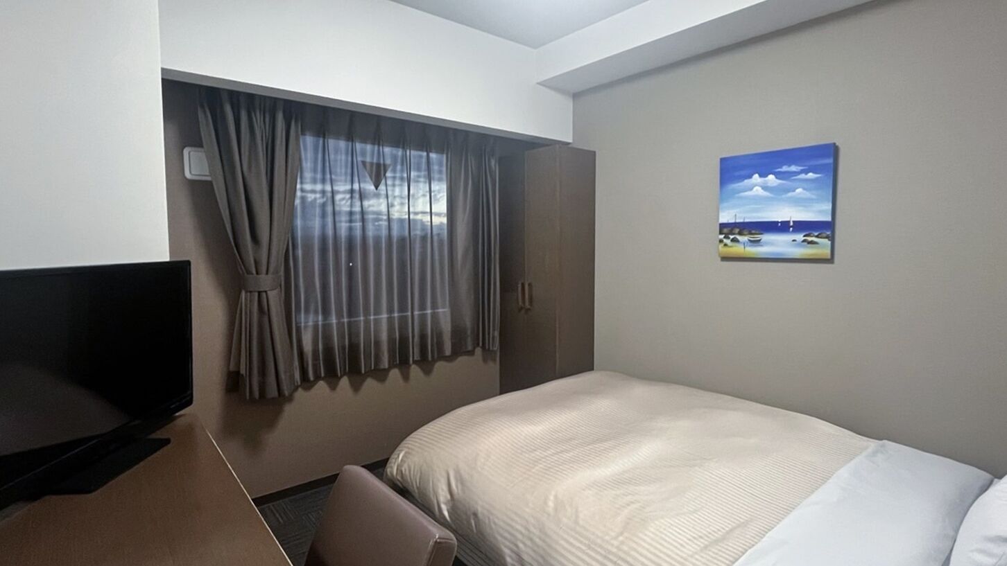 A hotel room with a bed, a TV, a window with curtains, and a painting on the wall.