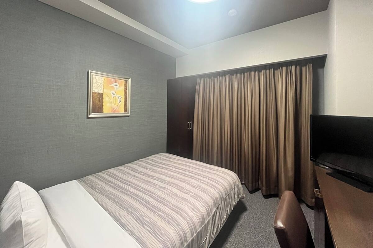 A hotel room with a bed, a television, a painting on the wall, and a curtain.