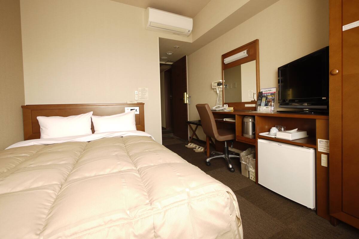 A hotel room with a bed, a desk, a chair, a television, and a mini-fridge.