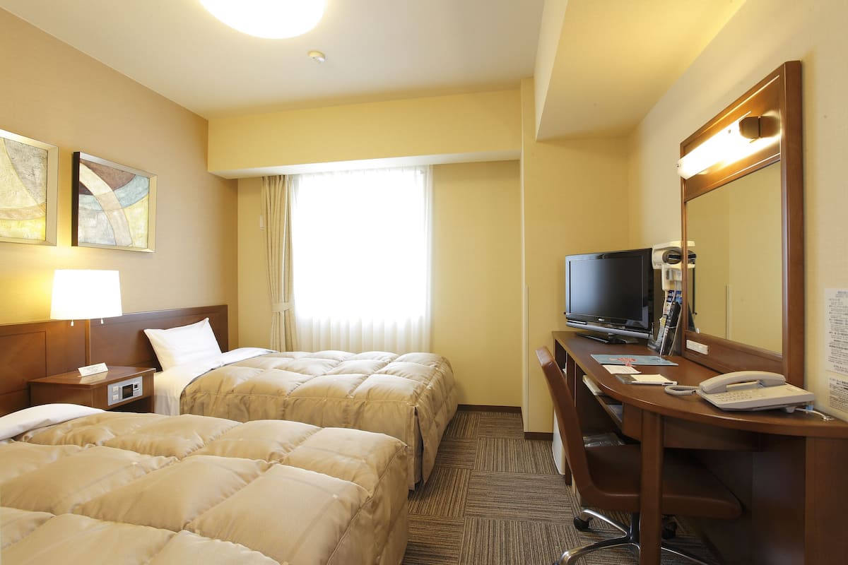 A hotel room with two beds, a desk with a computer, a telephone, and a television.