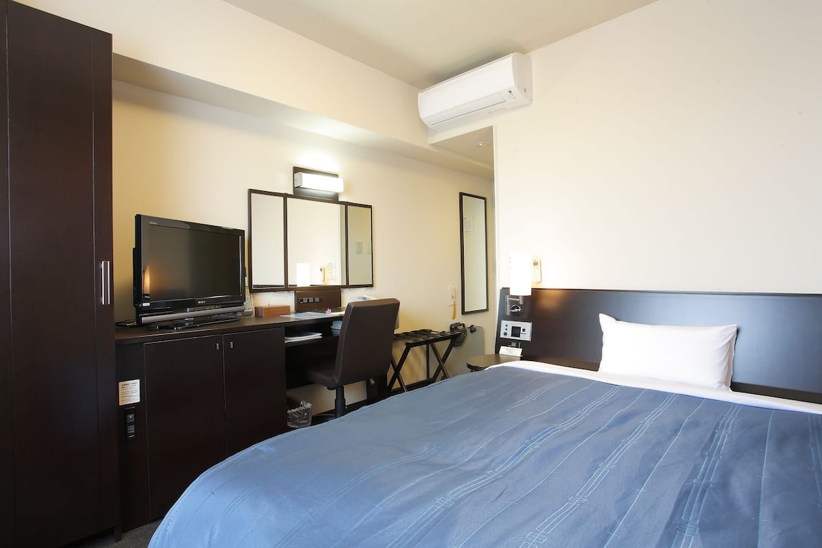 A hotel room with a bed, a desk with a computer, a television, and a wardrobe.