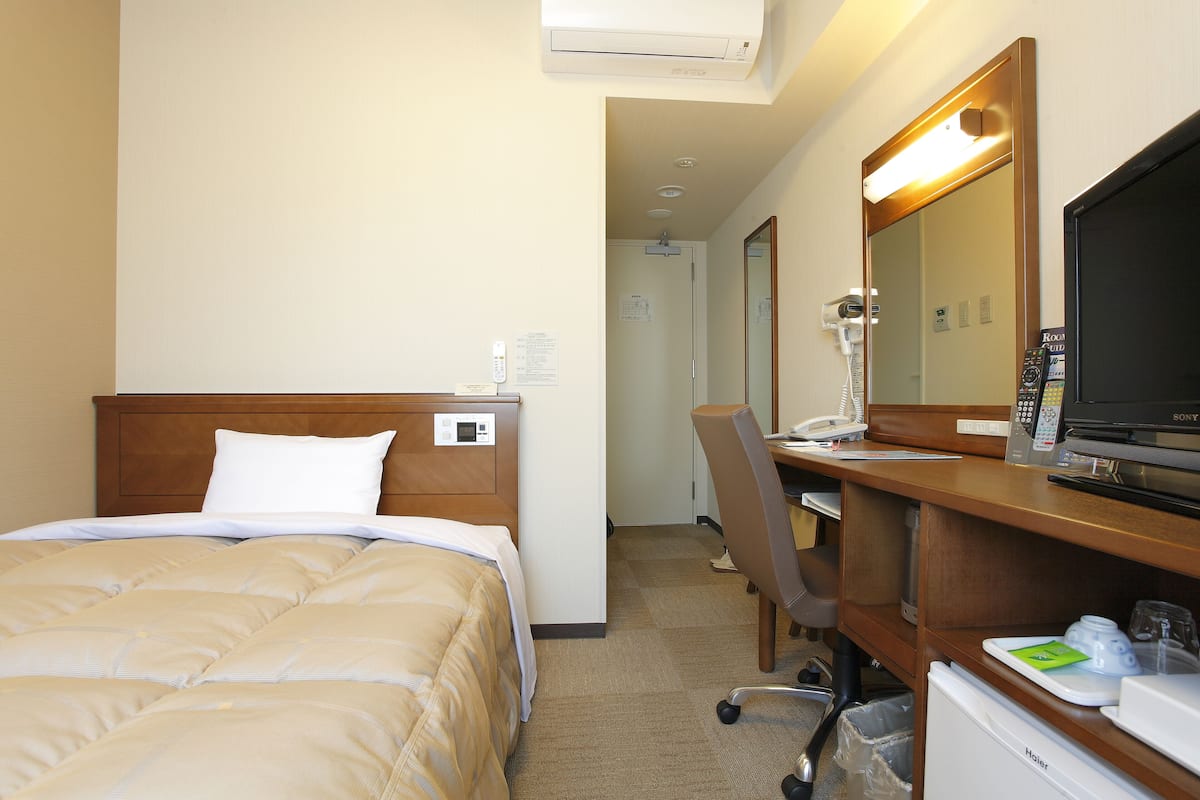 A hotel room with a bed, a desk with a computer, a mirror, and a TV.