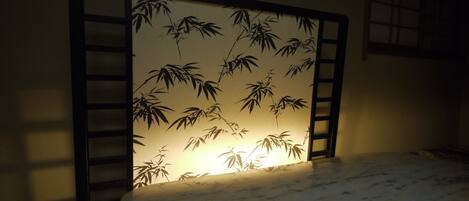 A room with a bed, a wall with a bamboo pattern, and a window with a grid design.