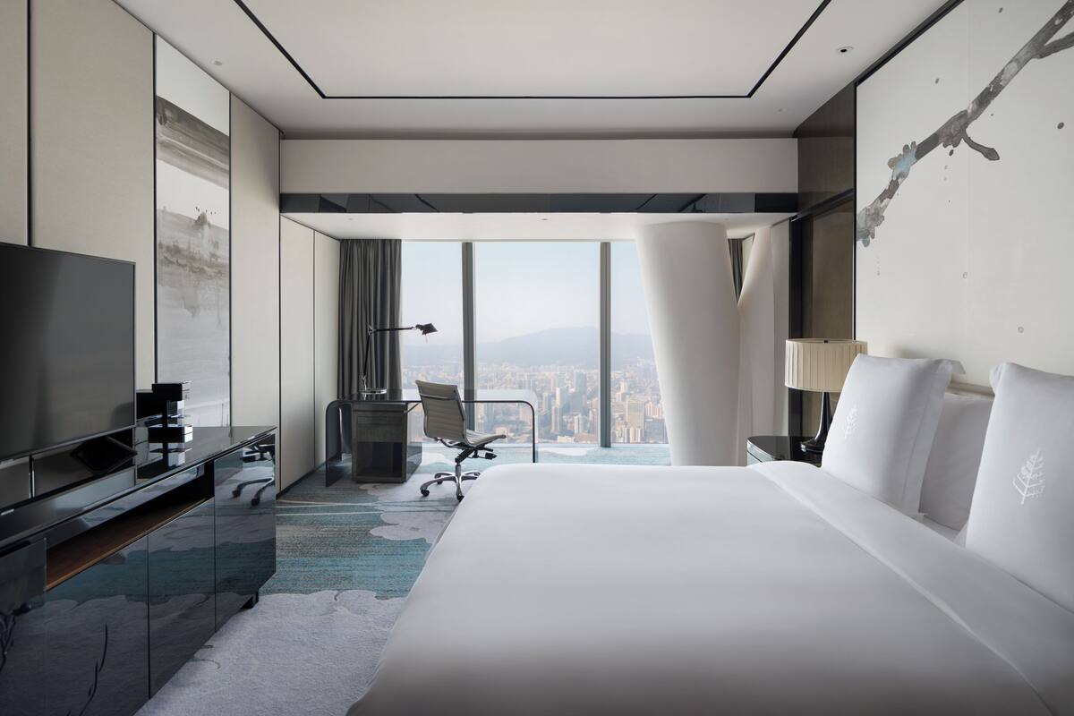 A modern hotel room with a large bed, a desk, a chair, and a television.