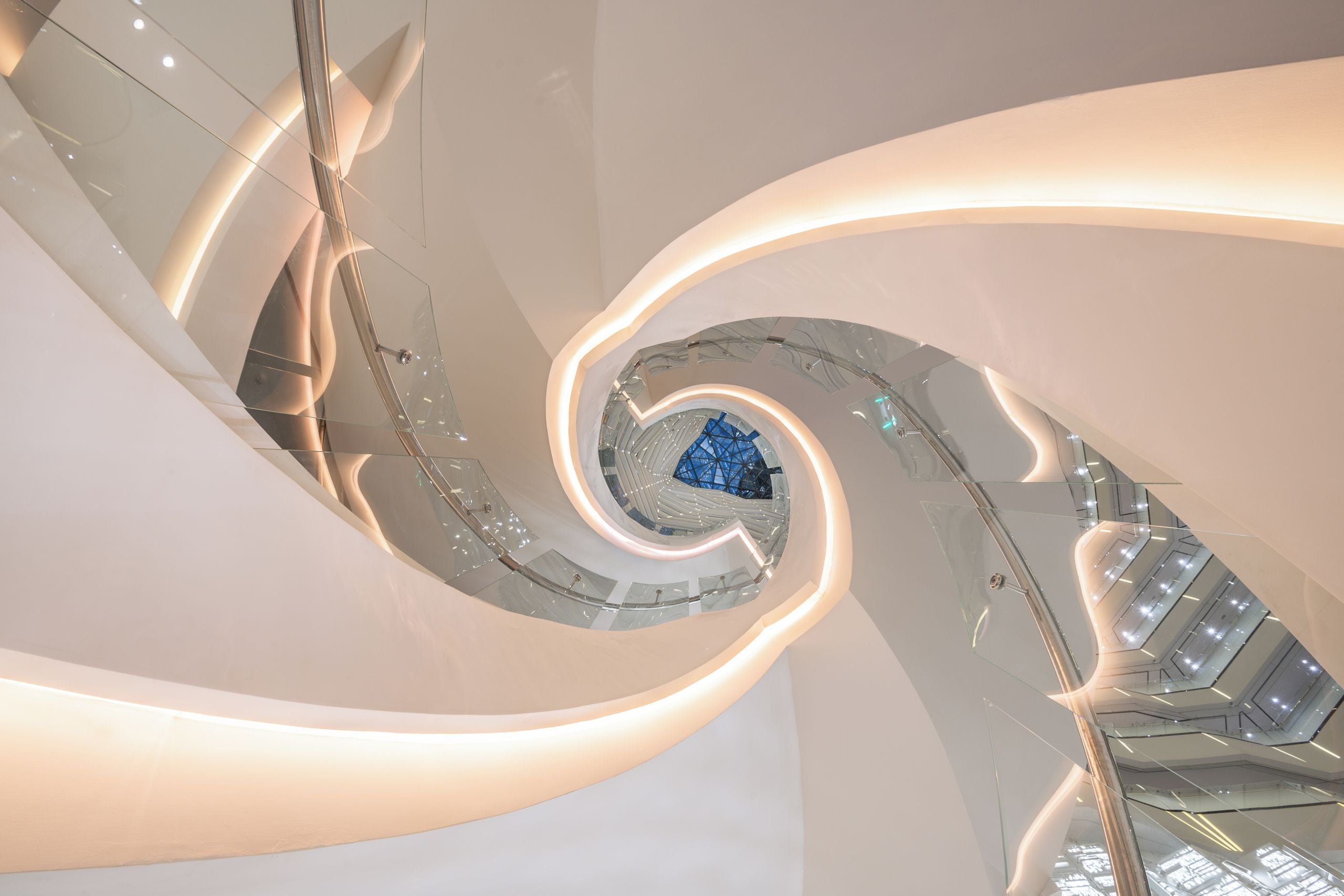 A spiral staircase with glass railings and a central blue geometric structure.